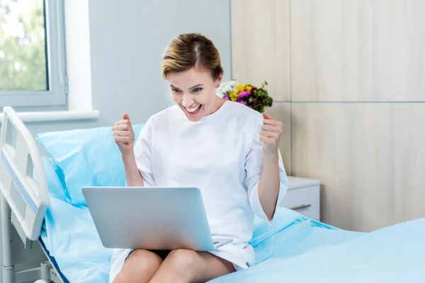 Mujer excitada gesto de la paciente por las manos y tener videollamada en el ordenador portátil en la habitación del hospital - foto de stock