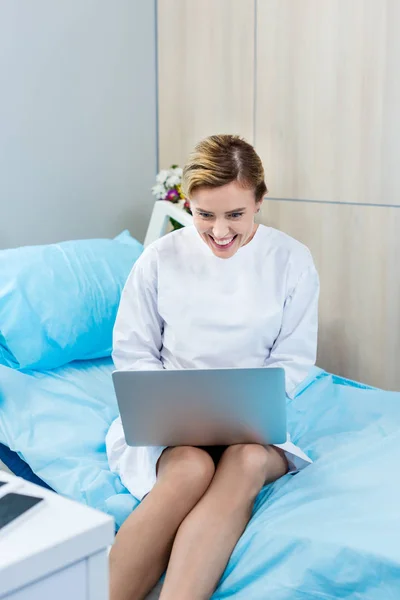 Paciente femenina feliz teniendo videollamada en la computadora portátil en la habitación del hospital - foto de stock