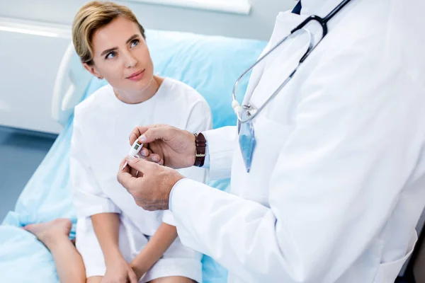 Partial view of male doctor checking thermometer near female patient in hospital room — Stock Photo