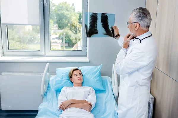 Pensive male doctor analyzing x-ray picture near female patient in hospital room — Stock Photo