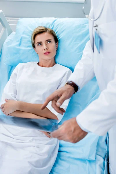 Abgeschnittenes Bild eines männlichen Arztes, der auf ein Röntgenbild einer Patientin im Krankenhauszimmer zeigt — Stockfoto