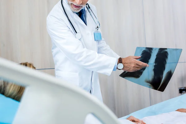 Vue partielle du médecin masculin pointant une image radiographique vers une patiente dans une chambre d'hôpital — Photo de stock