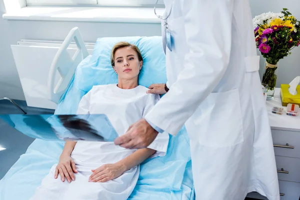 Imagen recortada de un médico varón sosteniendo una imagen de rayos X y animando a una paciente femenina en la habitación del hospital - foto de stock