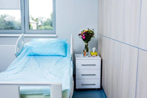 Intérieur de la chambre d'hôpital avec lit, fleurs et table de chevet — Photo de stock
