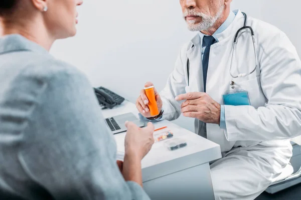 Partial view of mature male doctor pointing at pills to female patient at table in office — Stock Photo