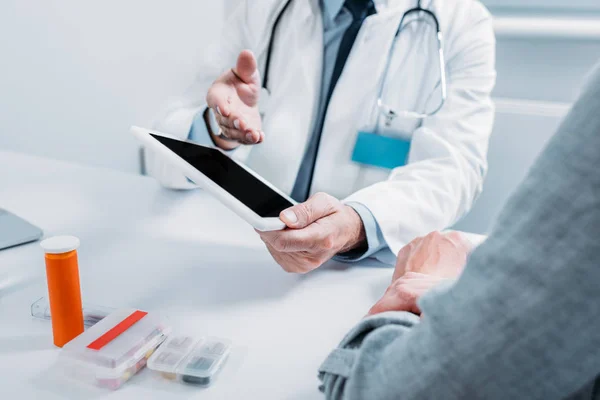 Vue partielle du médecin masculin pointant vers la tablette numérique avec écran blanc au patient féminin à la table au bureau — Photo de stock