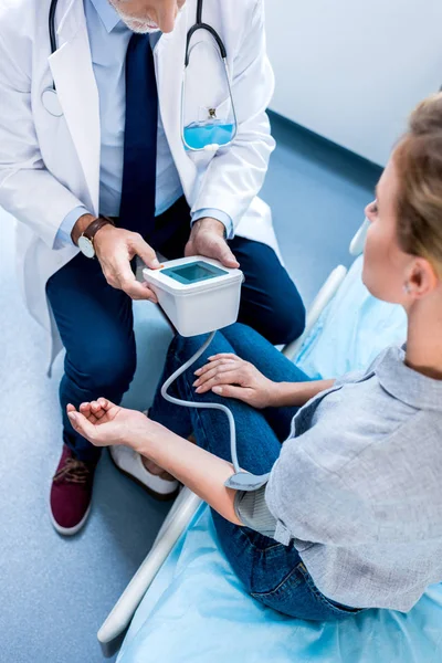 Partial view of male doctor with stethoscope measuring pressure of female patient by tonometer in hospital room — Stock Photo