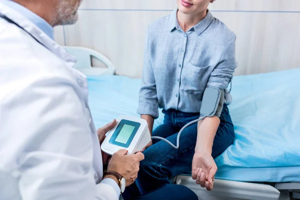 Частичный взгляд врача мужского пола, измеряющего давление женщины по тонометру в больничной палате — стоковое фото