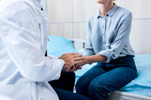 Imagen recortada de doctor masculino cogido de la mano de paciente femenino en la habitación del hospital - foto de stock