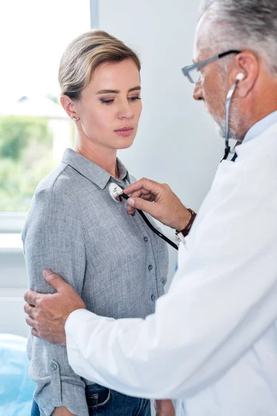 Mature male doctor examining female patient by stethoscope in hospital room — Stock Photo