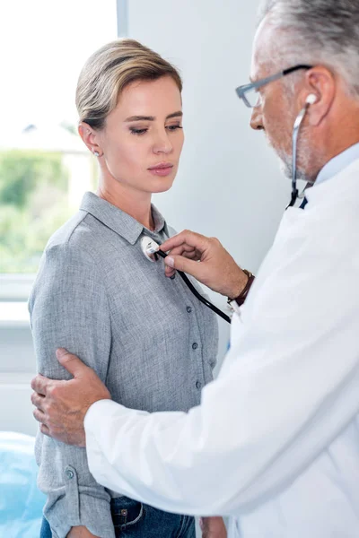 Maduro médico masculino examinando paciente feminino por estetoscópio no quarto do hospital — Fotografia de Stock