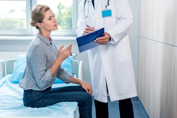 Cropped image of male doctor showing clipboard to female patient in hospital room — Stock Photo