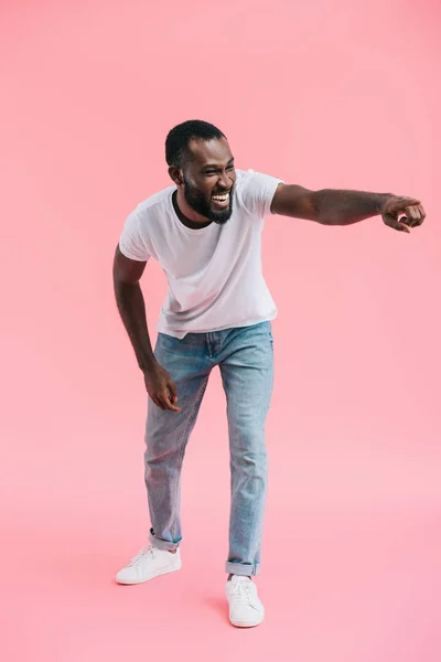 Joven afroamericano hombre riendo y señalando lejos en rosa fondo - foto de stock