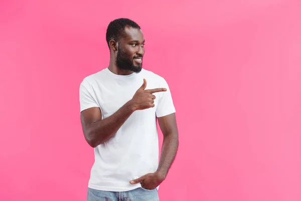 Portrait of young smiling african american man pointing away isolated on pink — Stock Photo