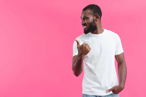 Retrato de un joven afroamericano sonriente apuntando aislado sobre rosa - foto de stock