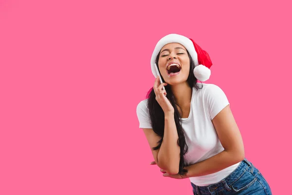 Portrait of happy african american woman in santa claus hat talking on smartphone isolated on pink — Stock Photo