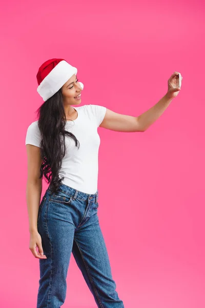 Seitenansicht einer lächelnden Afroamerikanerin mit Weihnachtsmann-Hut, die ein Selfie auf ihrem Smartphone macht, isoliert auf rosa — Stockfoto