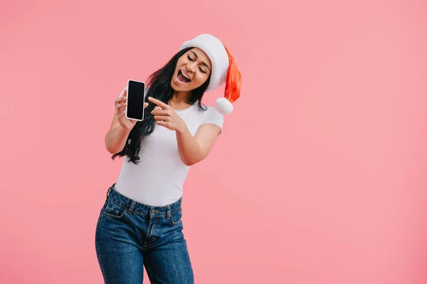 Retrato de mulher americana africana feliz em chapéu de santa claus apontando para smartphone com tela em branco isolado em rosa — Fotografia de Stock