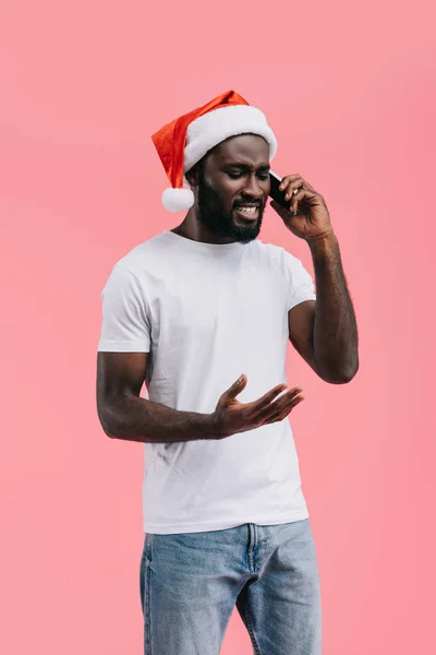 Sonriente afroamericano hombre en santa claus sombrero hablando en teléfono inteligente aislado en rosa - foto de stock