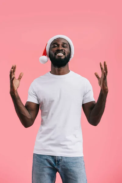Hombre afroamericano excitado con los brazos levantados en sombrero de Navidad aislado sobre fondo rosa - foto de stock