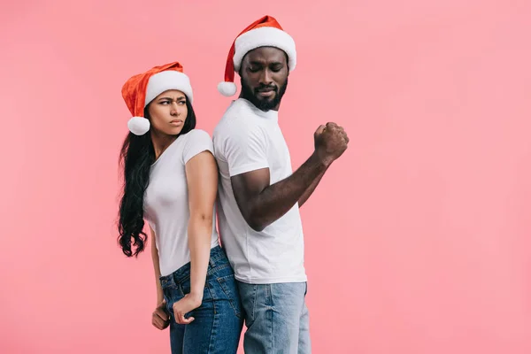 Angry african american woman in christmas hat standing back to back with boyfriend isolated on pink background — Stock Photo