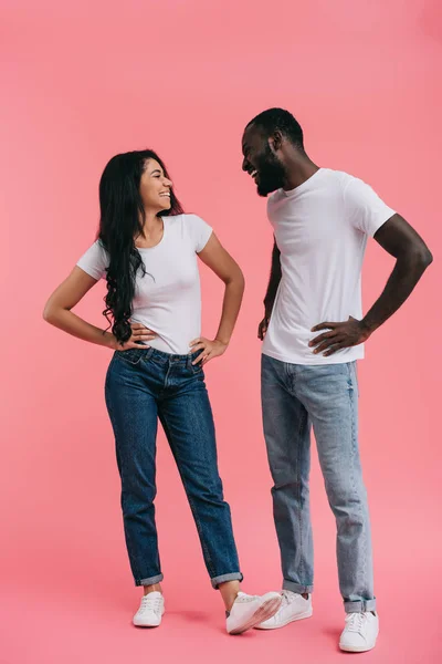 Rindo jovem casal afro-americano com as mãos na cintura olhando uns para os outros isolado no fundo rosa — Fotografia de Stock