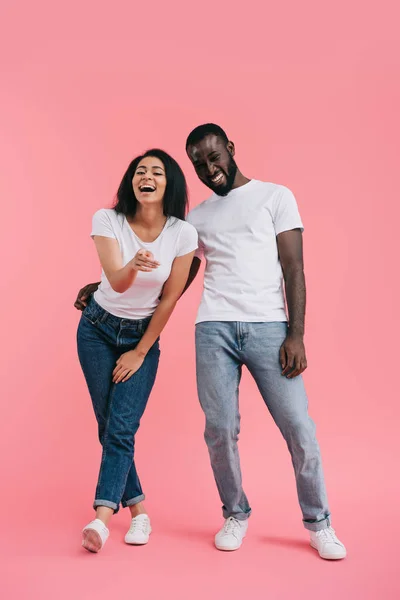 Смеющаяся африканская американка указывает на камеру с парнем, стоящим рядом на розовом фоне — стоковое фото