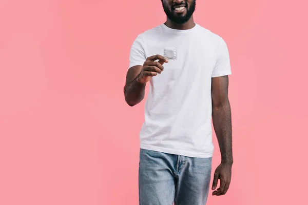 Partial view of young african american man with condom isolated on pink background — Stock Photo