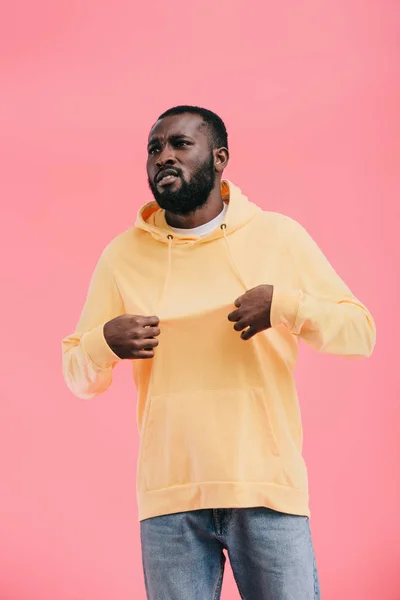 Upset african american man showing yellow hoodie on himself isolated on pink background — Stock Photo