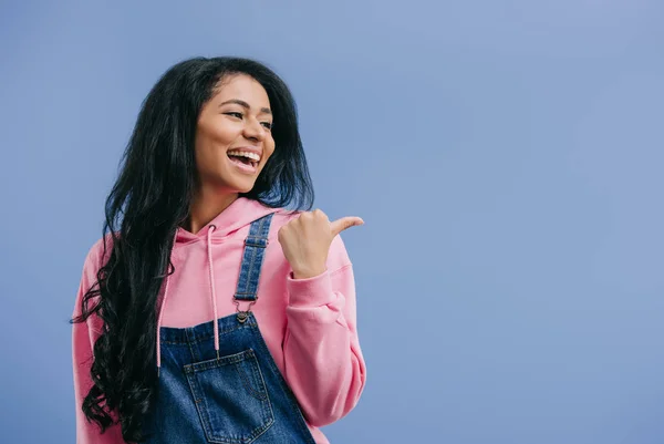 Sorridente giovane donna afroamericana che punta a parte dal dito isolato su sfondo blu — Foto stock