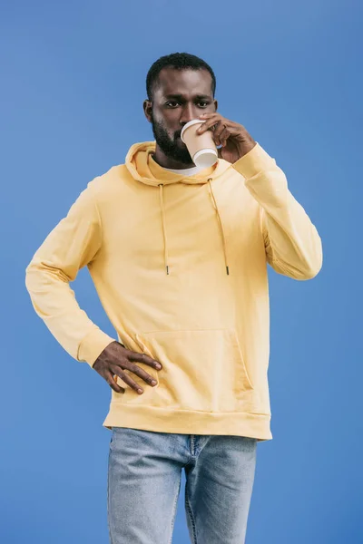 Selbstbewusster junger afrikanisch-amerikanischer Mann trinkt Kaffee aus Pappbecher isoliert auf blauem Hintergrund — Stockfoto