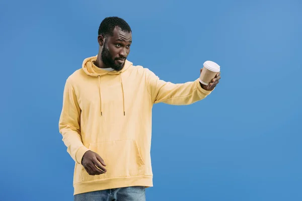 Giovane uomo africano americano che offre tazza di caffè usa e getta isolato su sfondo blu — Foto stock