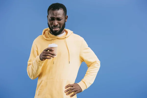 Deluso giovane uomo africano americano con tazza di caffè usa e getta isolato su sfondo blu — Foto stock