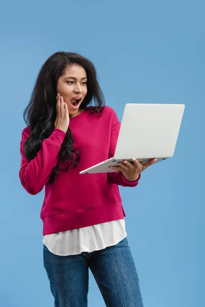 Mujer afroamericana sorprendida sosteniendo portátil aislado sobre fondo azul - foto de stock