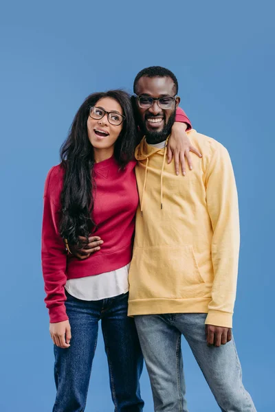 Stylish happy african american couple in eyeglasses embracing each other isolated on blue background — Stock Photo