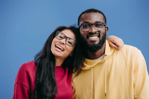 Retrato de feliz pareja afroamericana en gafas mirando a la cámara aislada sobre fondo azul - foto de stock