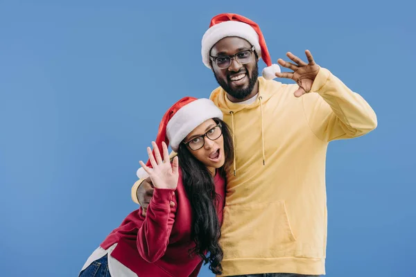 Улыбающаяся африканская американская пара в рождественских шляпах, машущая руками на голубом фоне — стоковое фото