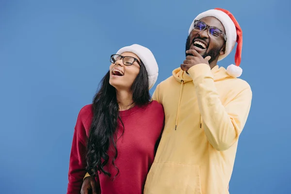Rindo casal afro-americano em chapéus de Natal e óculos isolados em fundo azul — Fotografia de Stock