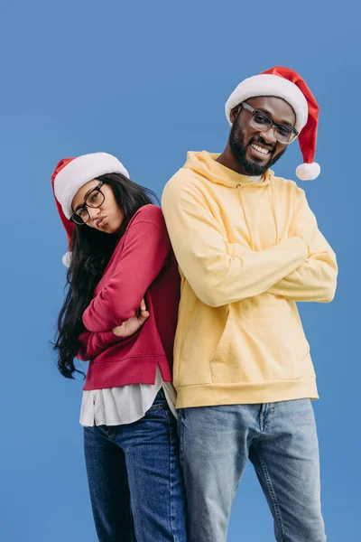 Elegante casal afro-americano em chapéus de Natal de pé com braços cruzados isolados em fundo azul — Fotografia de Stock