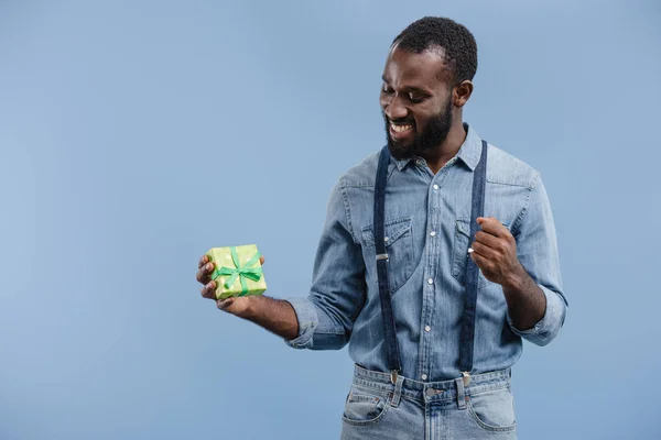 Щасливий молодий афроамериканський чоловік з подарунковою коробкою, загорнутий жестом стрічки рукою ізольований на синьому фоні — стокове фото