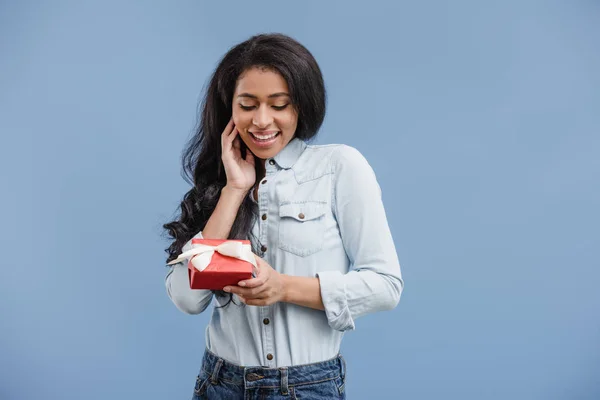 Atractiva mujer afroamericana elegante sosteniendo caja de regalo aislado sobre fondo azul - foto de stock