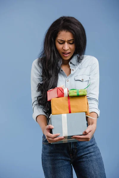 Chica afroamericana insatisfecha mirando cajas de regalo aisladas en azul - foto de stock