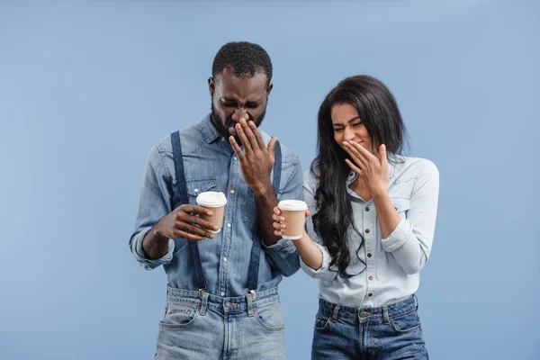 Grimacing african american couple holding coffee to go and covering noses isolated on blue — Stock Photo