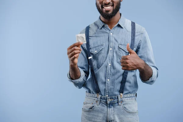 Cropped image of smiling african american man showing thumb up to condom isolated on blue — Stock Photo