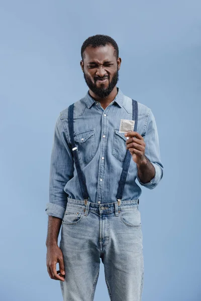 Homem afro-americano sorridente segurando preservativo isolado em azul — Fotografia de Stock