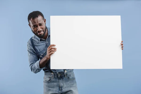 Sad african american man holding blank placard isolated on blue — Stock Photo