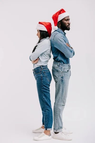 Irritated african american couple in santa hats standing back to back with crossed arms isolated on white — Stock Photo
