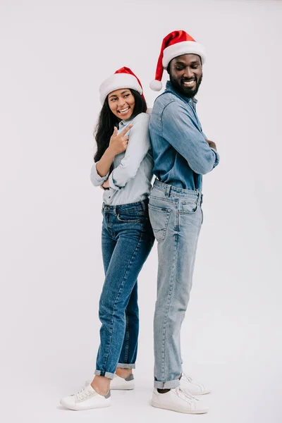 Sorridente coppia afroamericana in cappelli di Babbo Natale in piedi schiena isolata su bianco — Foto stock