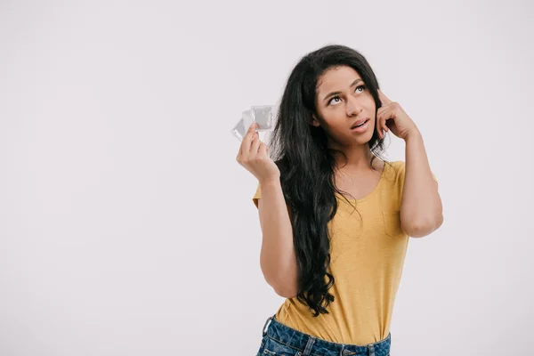 Pensive attractive african american girl holding latex condoms and looking up isolated on white — Stock Photo