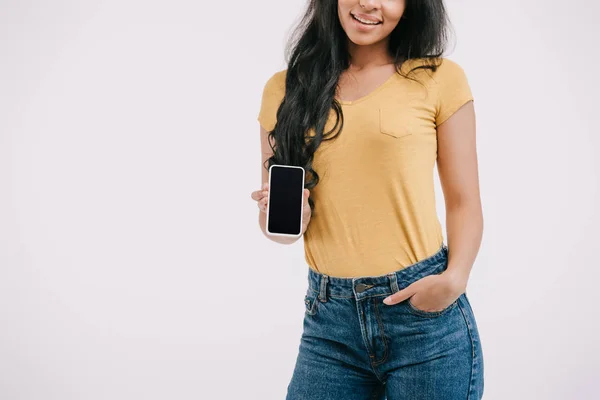 Обрезанное изображение улыбающейся африканской девушки, показывающей смартфон с пустым экраном, изолированным на белом — стоковое фото